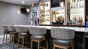 A bar area with a long counter, multiple stools, and a variety of liquor bottles.