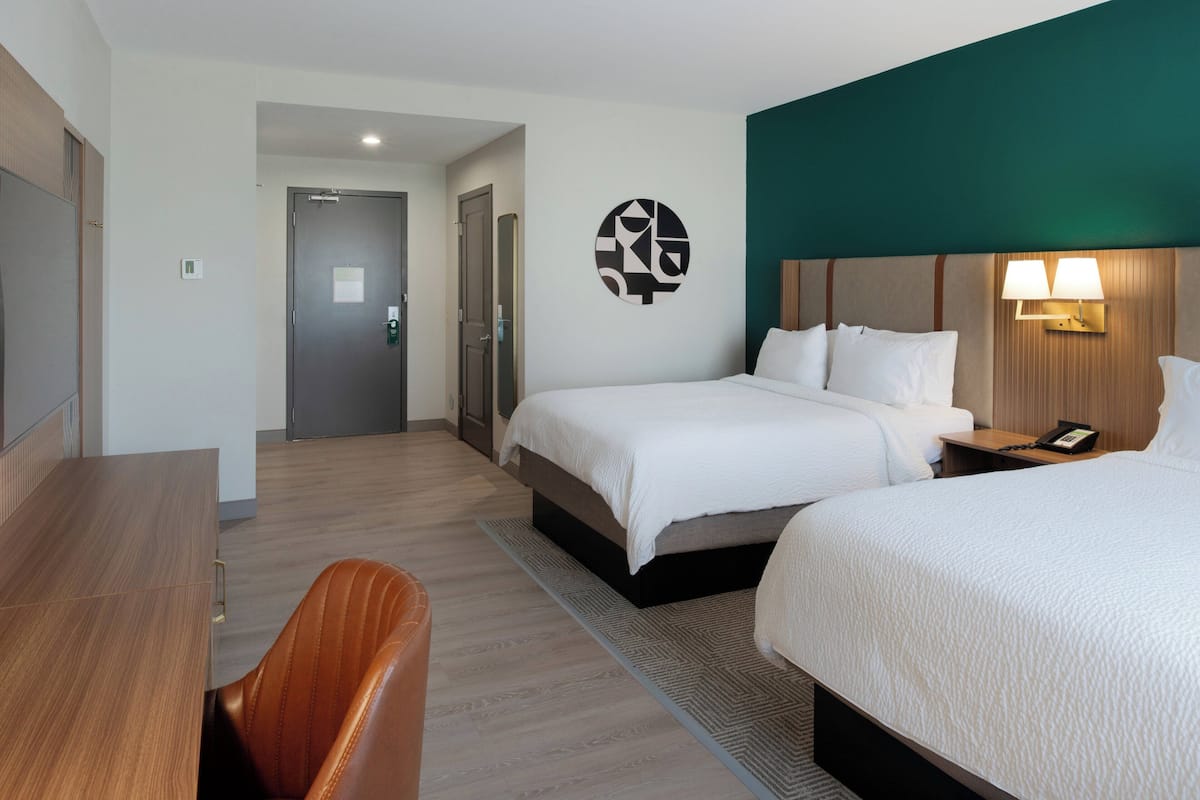 A hotel room with a bed, bedside table, lamp, and a desk with a chair.