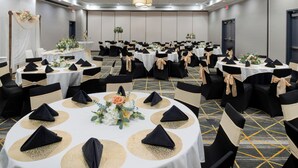 Un salón de conferencias con mesas redondas, sillas negras y manteles blancos.
