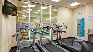 Un gimnasio con cintas de correr, una bicicleta estática y una pantalla de televisión.