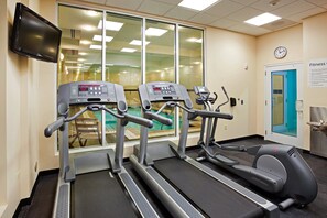 Uma sala de ginástica com esteiras, bicicleta ergométrica e uma tela de televisão.