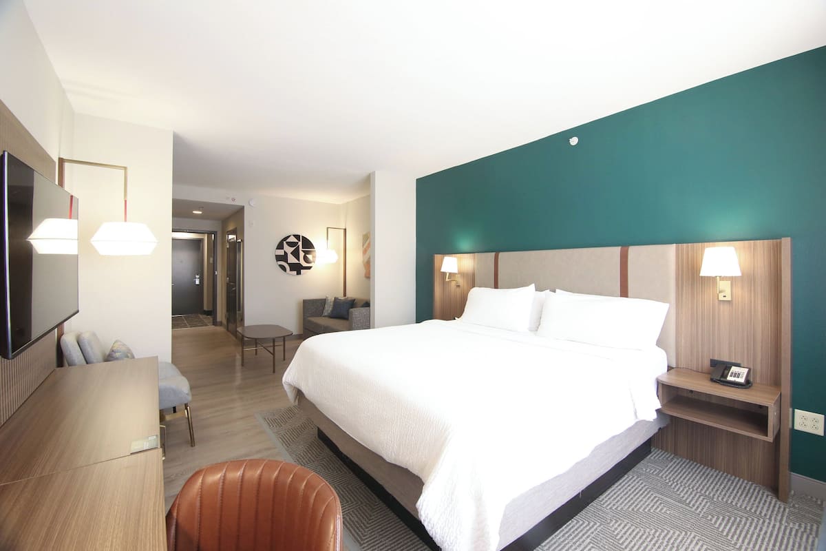 A hotel room with a large bed, a desk, a chair, and a TV.