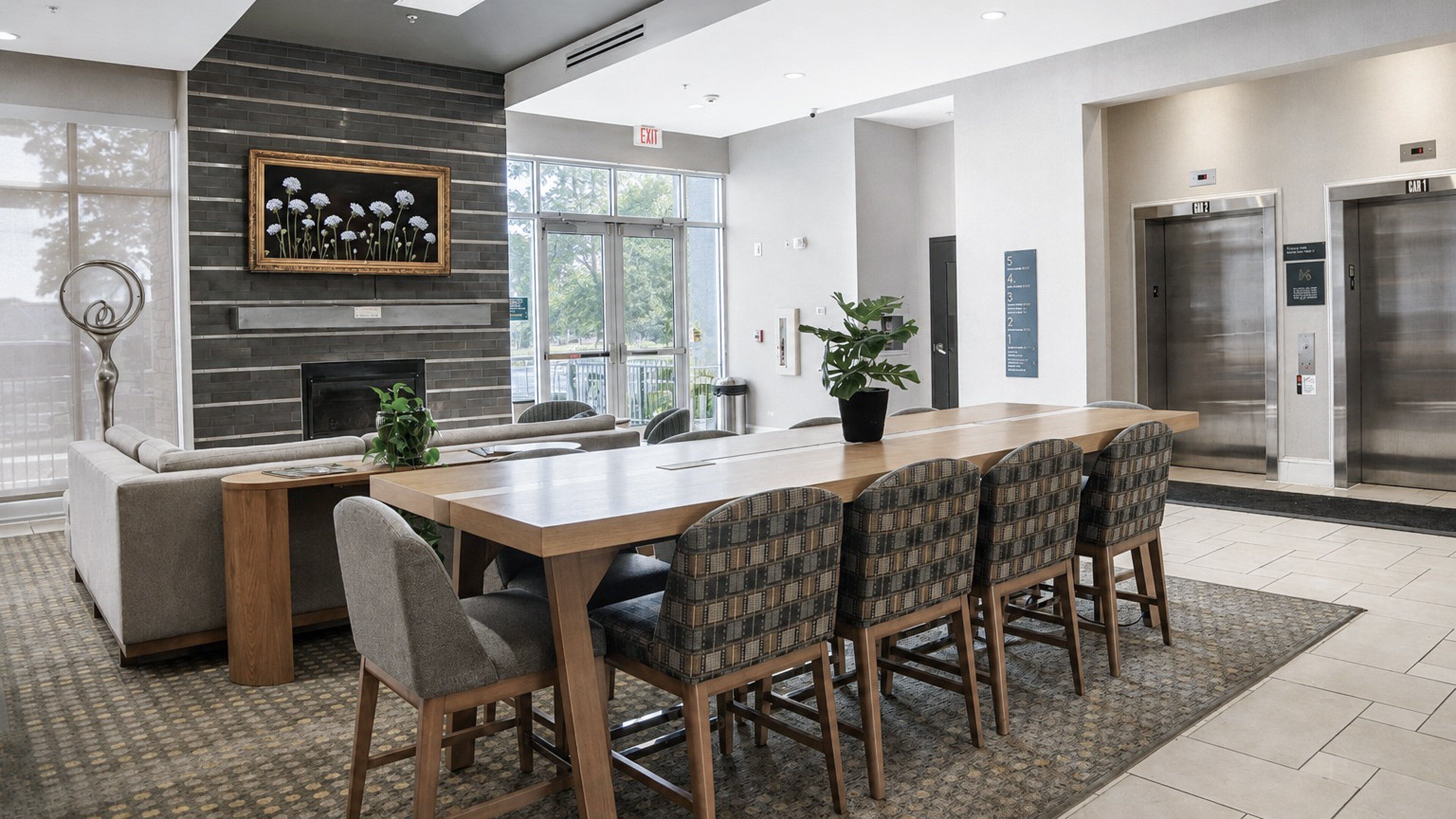 A modern conference room with a long table, chairs, a fireplace, and an exit sign.