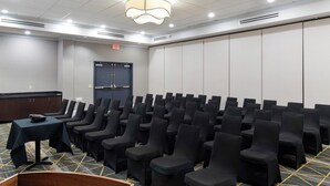 Un salón de conferencias con filas de sillas negras, un atril de madera y suelo alfombrado.
