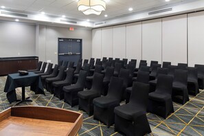 Uma sala de conferências com fileiras de cadeiras pretas, um púlpito de madeira e piso coberto de carpete.