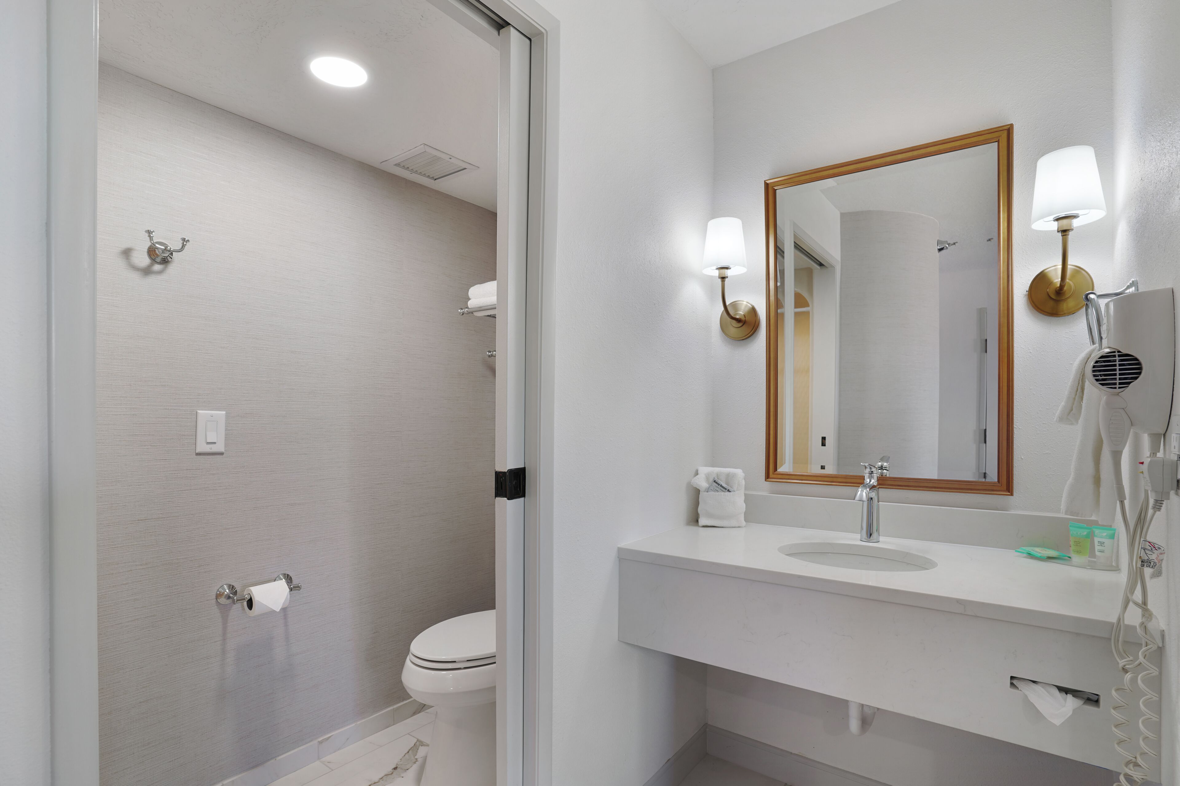 Un baño con inodoro, lavabo, espejo, toallero y secador de pelo.