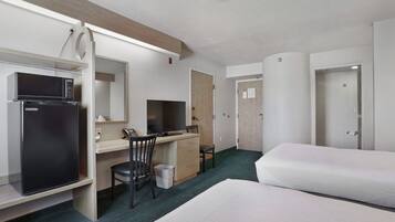 Ein Hotelzimmer mit Bett, Schreibtisch mit Computer, Mikrowelle, Stuhl und Mülleimer.