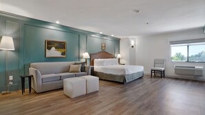 Moderni hotellihuone, jossa on sänky, sohva, tuoli ja pieni pöytä.