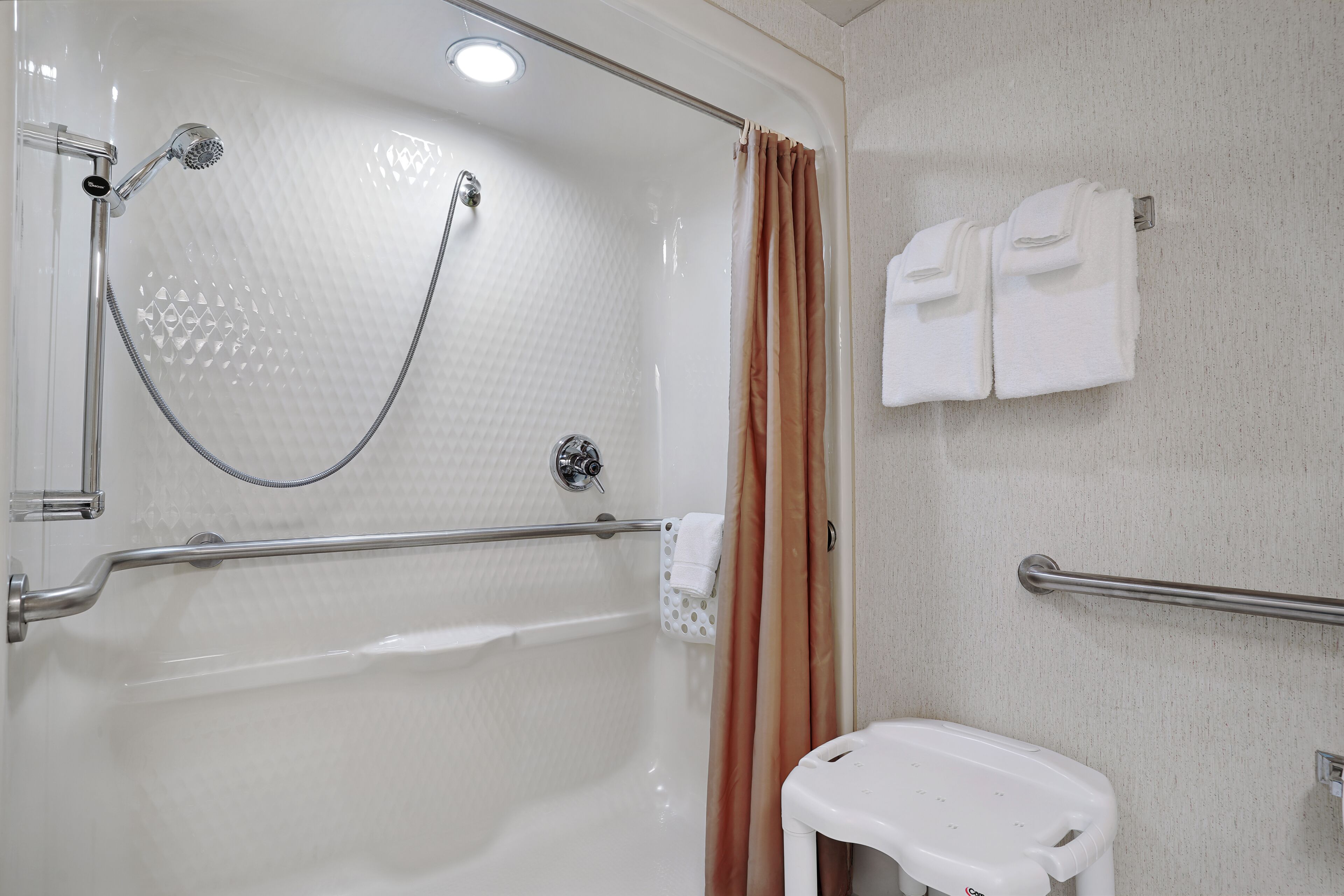 A bathroom with a shower, grab bars, a toilet, and towels.