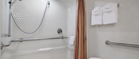 A bathroom with a shower, grab bars, a toilet, and towels.