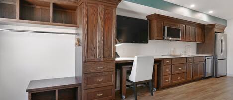 A kitchen with wooden cabinets, a built-in microwave, a refrigerator, and a bench.
