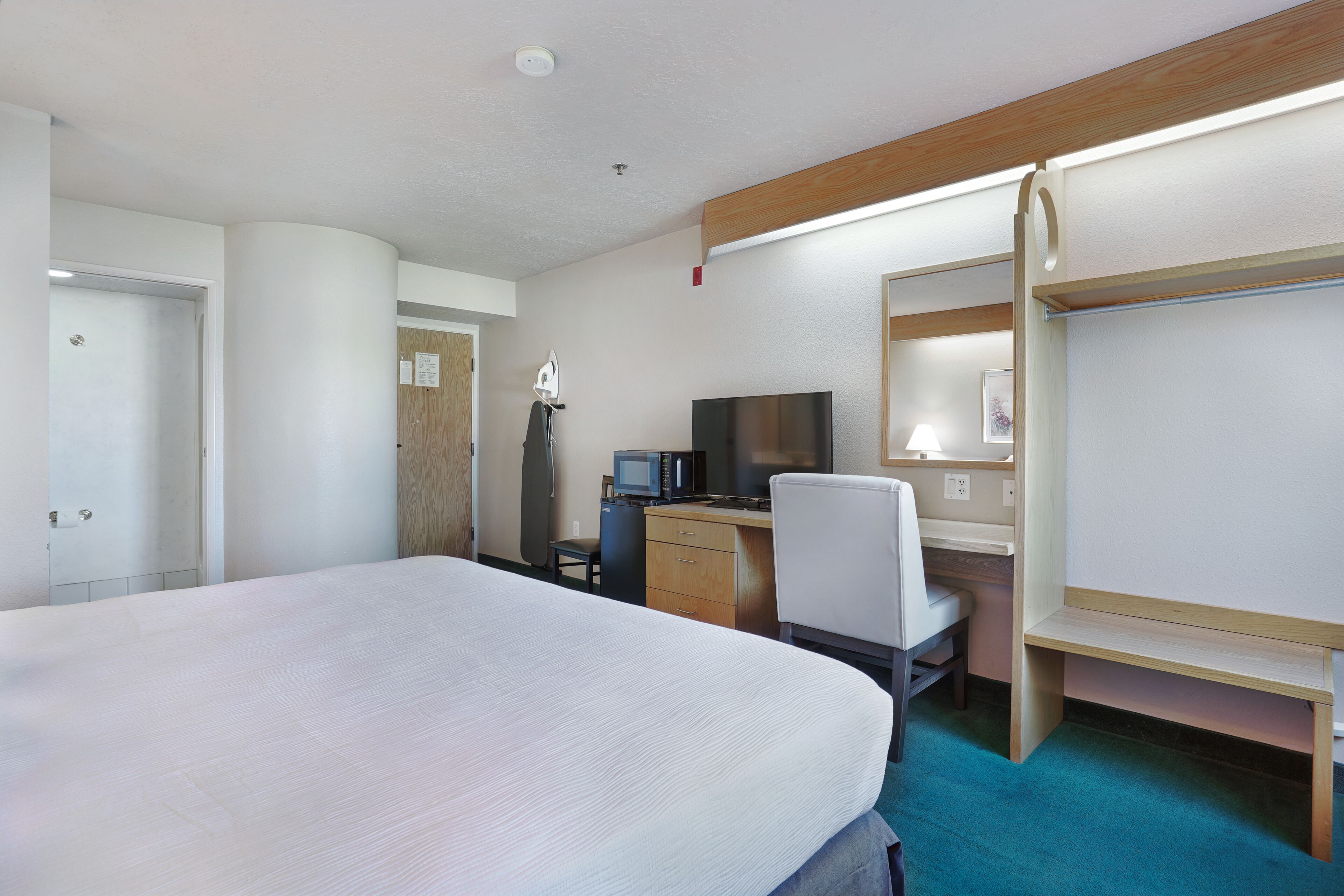 A hotel room with a large bed, a desk with a computer, a TV, and a chair.