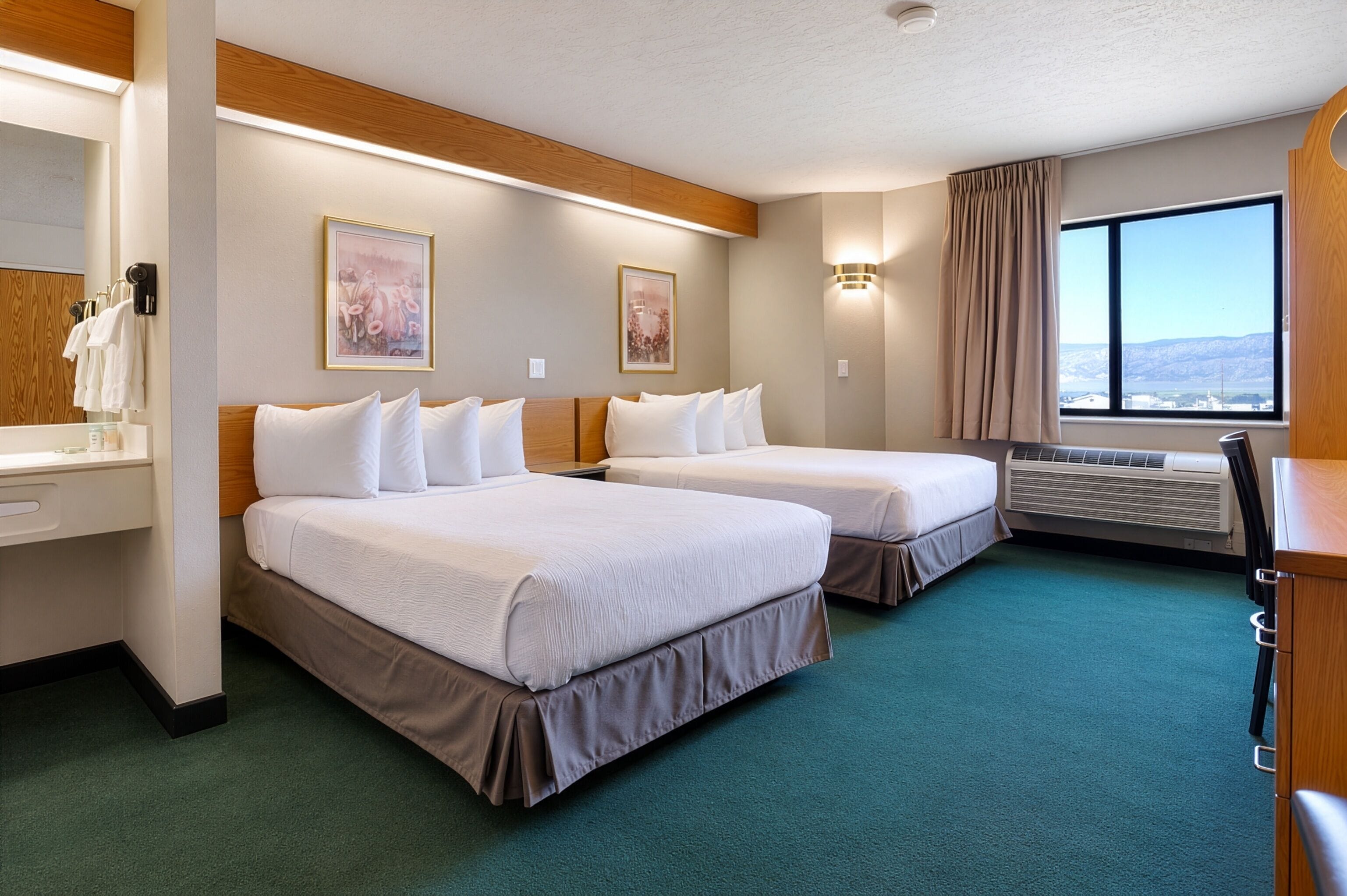 Een hotelkamer met twee bedden, een bureau, een spiegel en een raam met uitzicht.