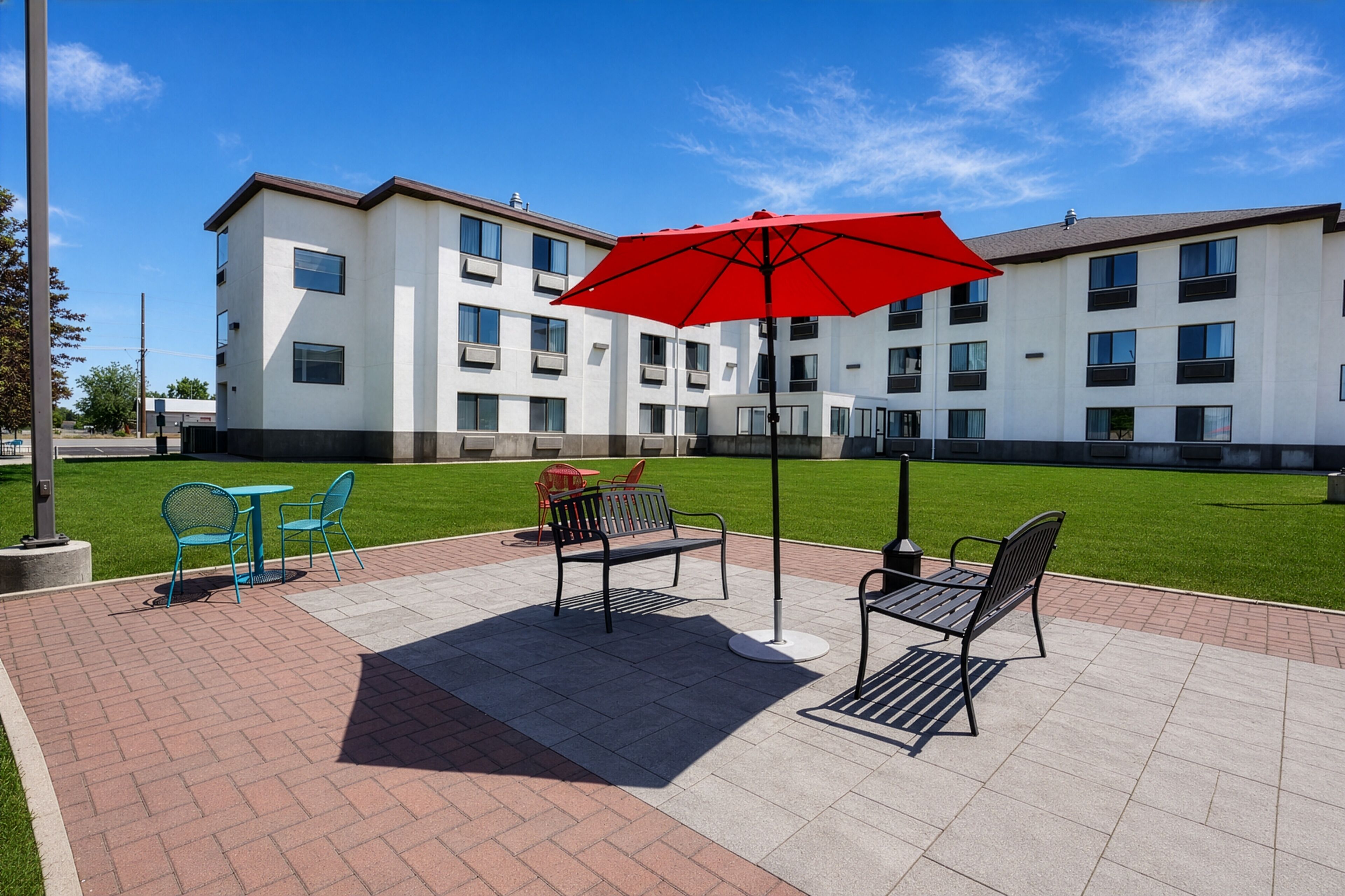 A courtyard with outdoor seating, a red umbrella, and a building in the background.