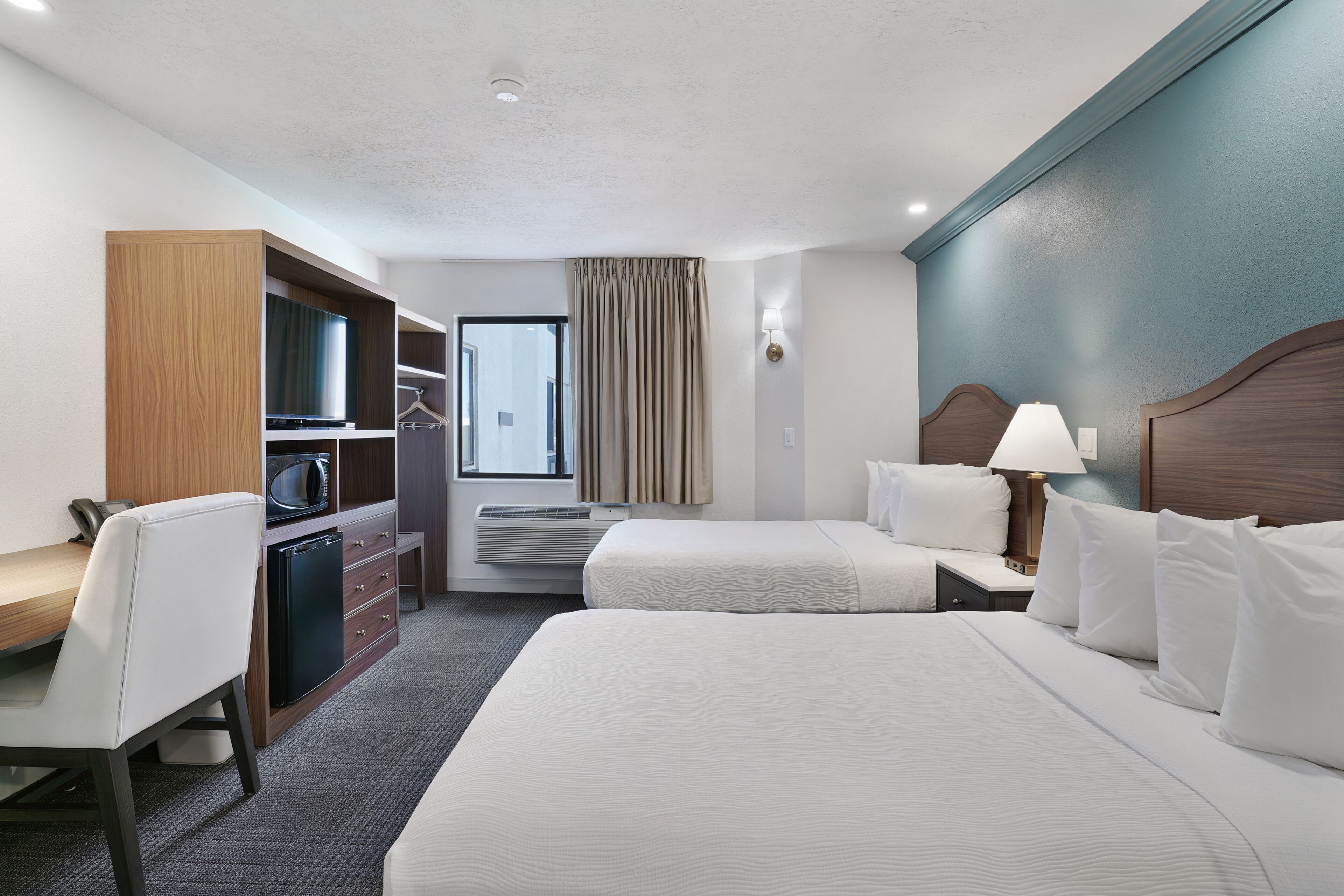 Une chambre d’hôtel avec deux lits, un bureau, un four à micro-ondes, un mini-réfrigérateur, une armoire et une fenêtre avec des rideaux.
