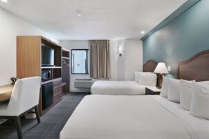Habitación de hotel con dos camas, un escritorio, microondas, refrigerador pequeño, armario y ventana con cortinas.