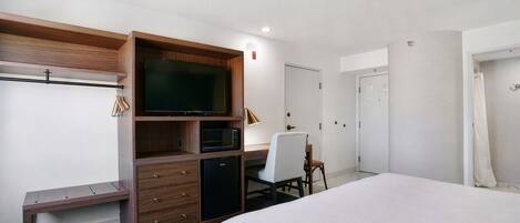 A hotel room with a bed, a desk with a chair, a television, a microwave, and a wardrobe.