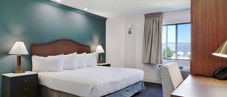 A hotel room with a large bed, two bedside tables with lamps, a desk with a telephone, a chair, and a window with a view.