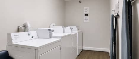 A laundry room with white appliances, a black trash bin, and a wooden floor.