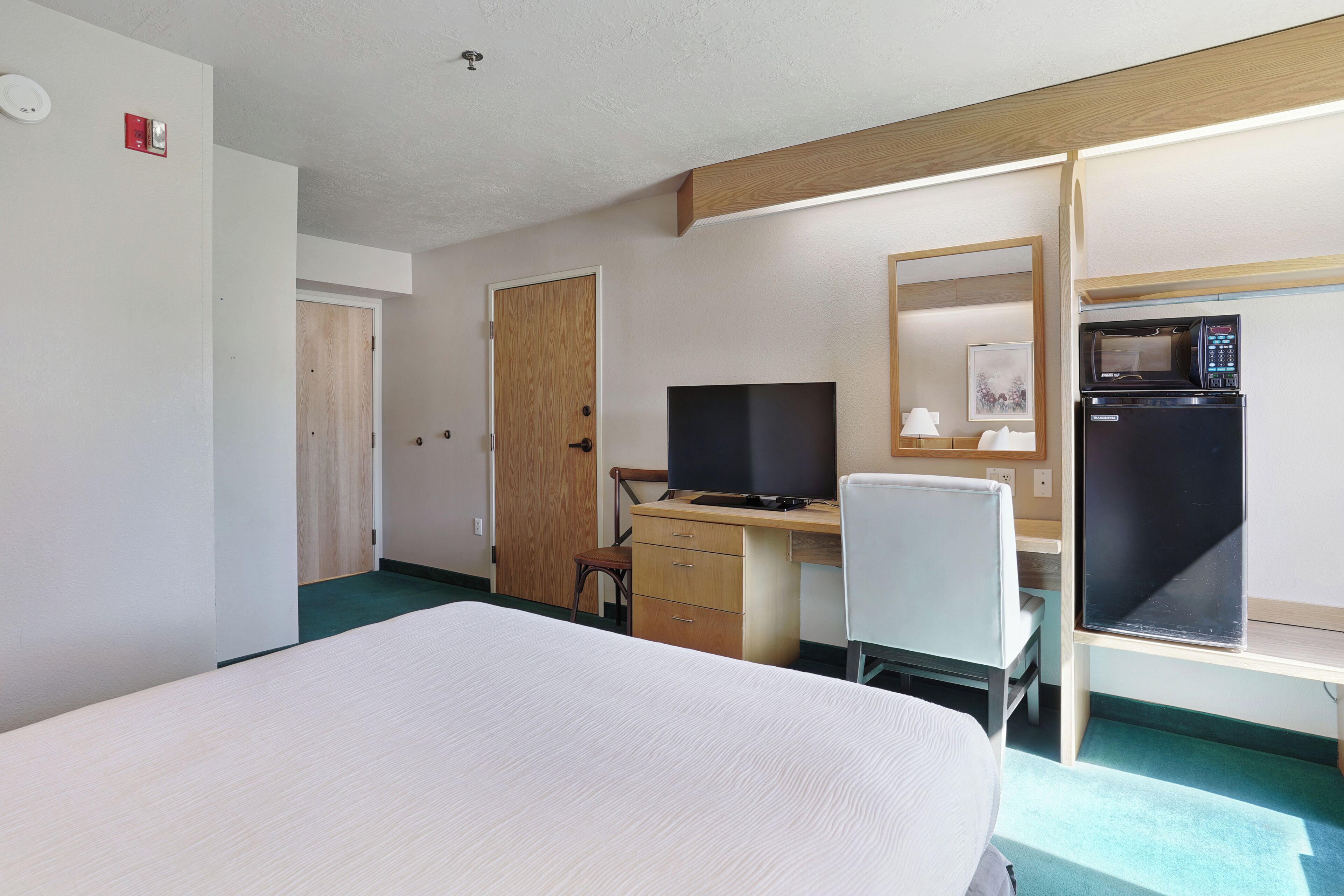 Ein Hotelzimmer mit einem Bett, einem Schreibtisch mit Computer, einem Stuhl, einer Mikrowelle und einem Kühlschrank.