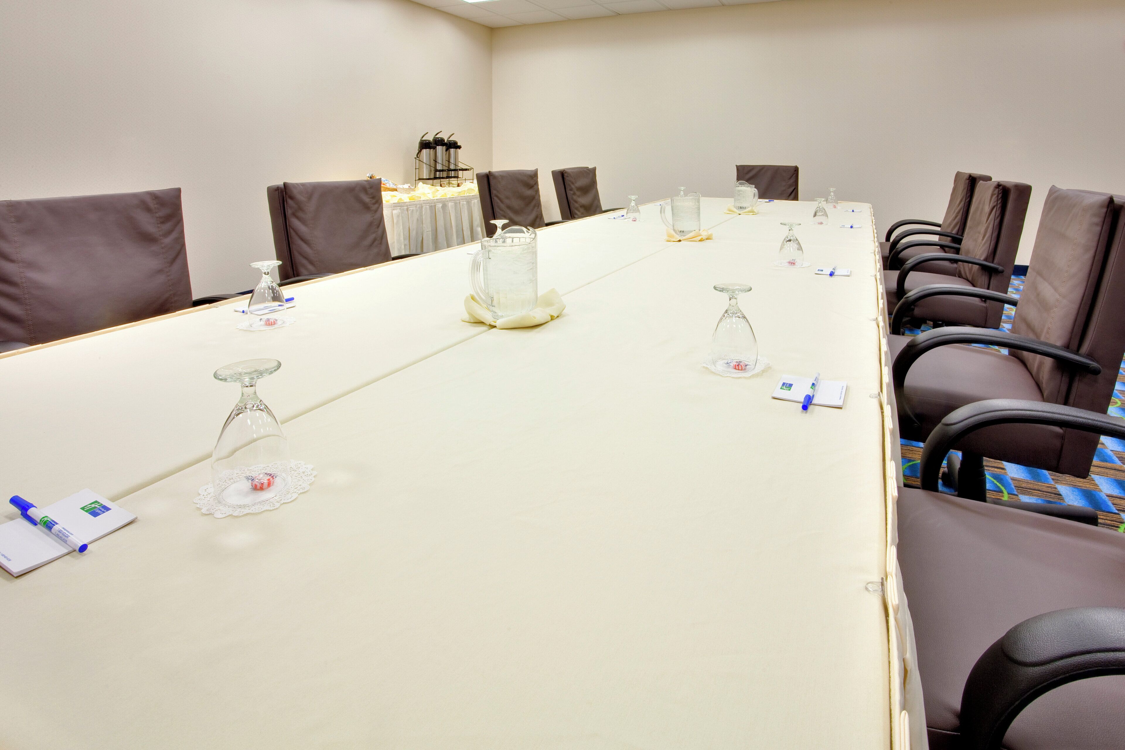 Une salle de conférence équipée d’une longue table, de chaises et de divers accessoires, comme des carafes d’eau, des verres et des blocs-notes.