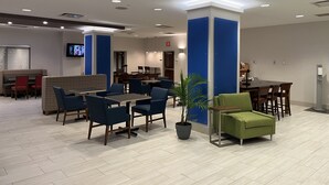 A modern hotel lobby with a seating area, a television, and a reception desk.