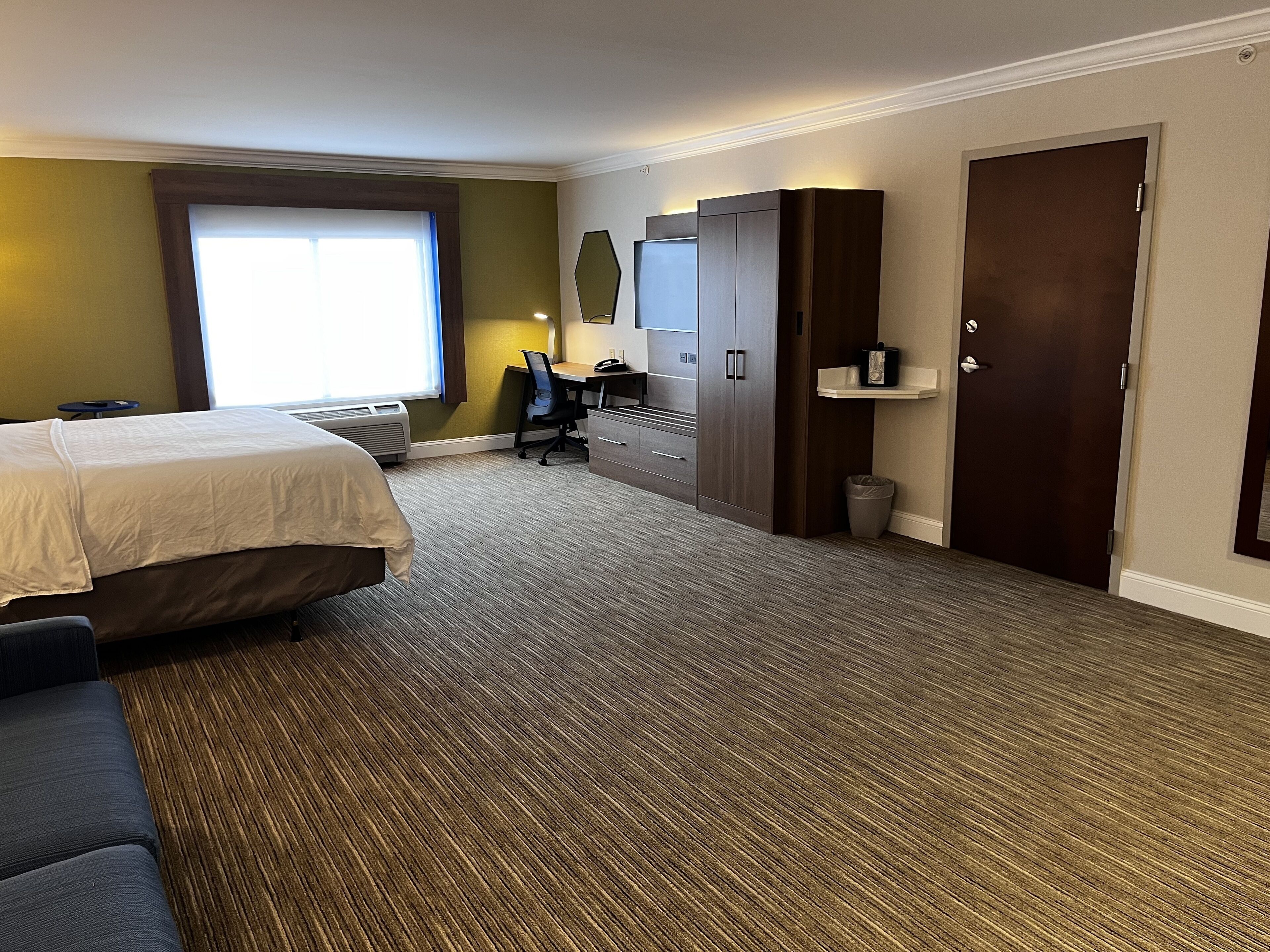 A hotel room with a bed, a desk, a chair, a wardrobe, and a door.