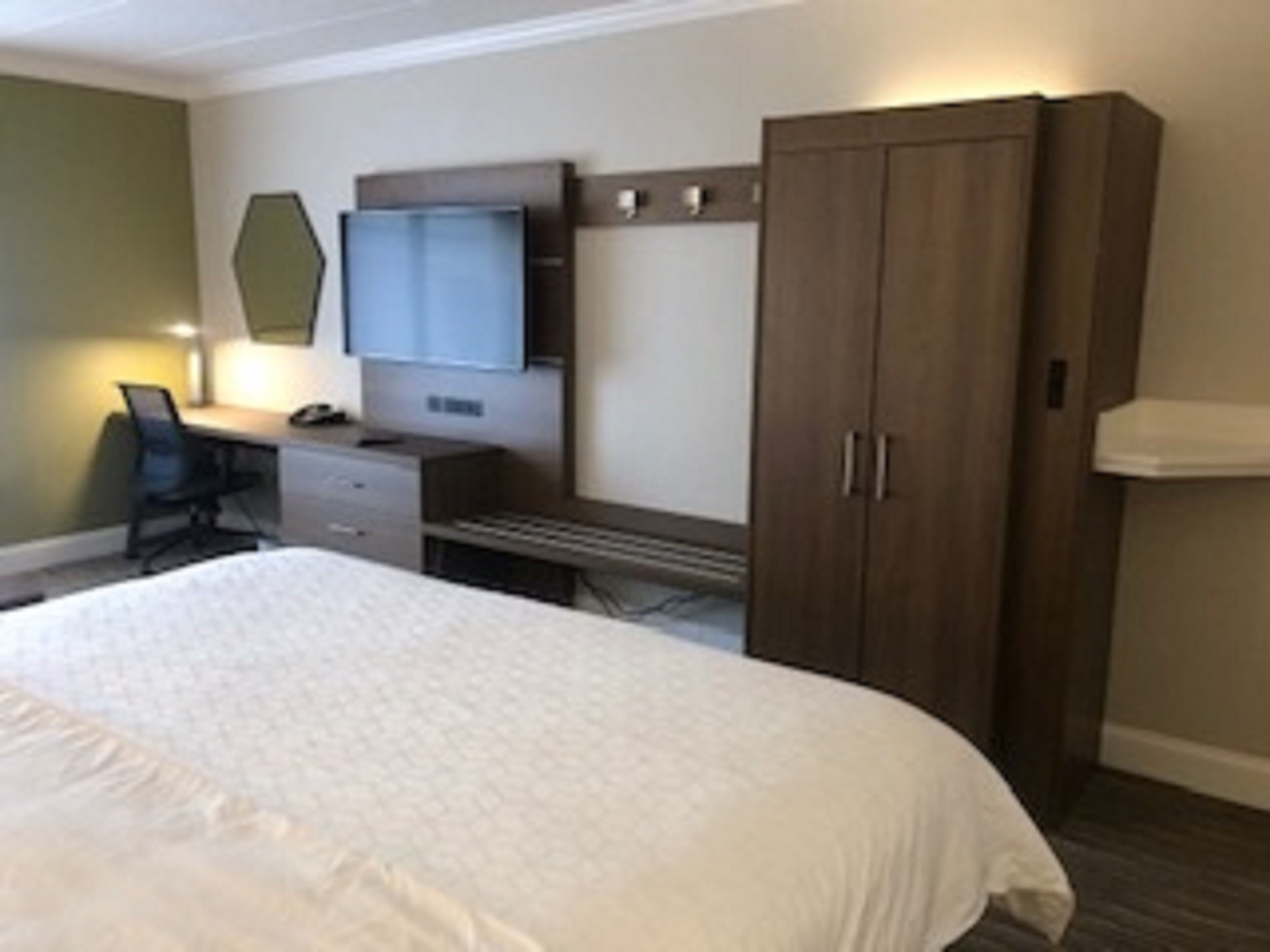 Una habitación de hotel con cama, escritorio, silla, armario y televisor.