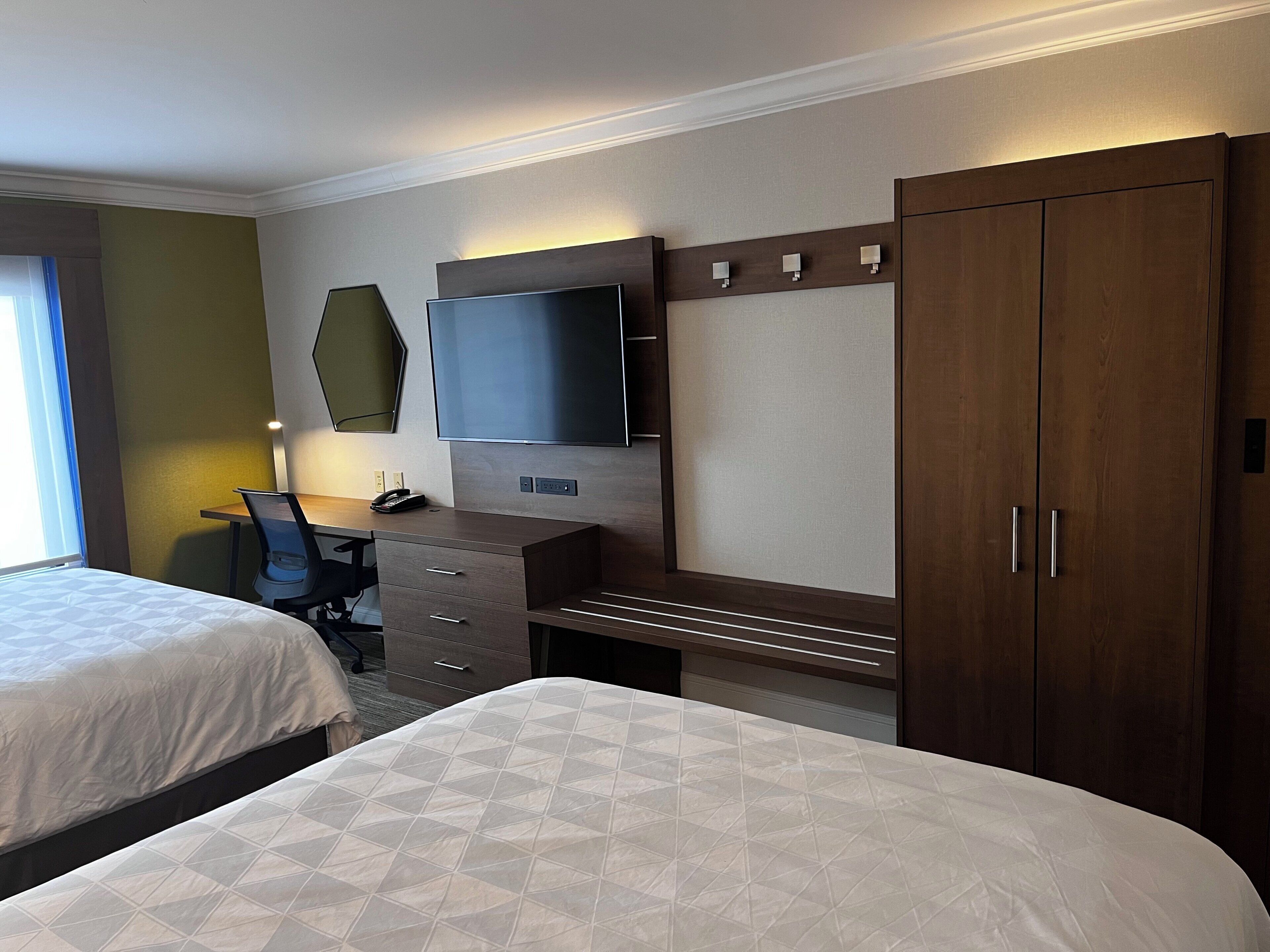Ein Hotelzimmer mit zwei Betten, einem Schreibtisch, einem Flachbildfernseher und einem Kleiderschrank.