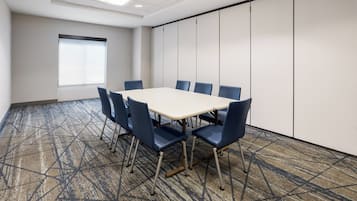Un salón de conferencias con una gran mesa y seis sillas, una ventana con persianas y una alfombra estampada.