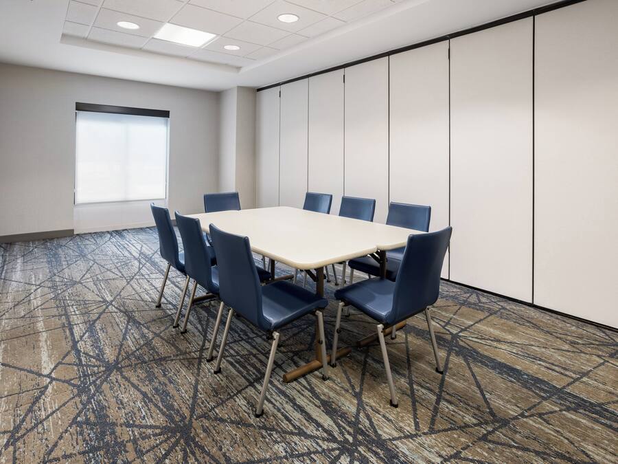 Un salón de conferencias con una gran mesa y seis sillas, una ventana con persianas y una alfombra estampada.
