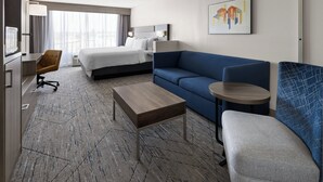 A hotel room with a bed, a sofa, a small table, a desk, and a chair.