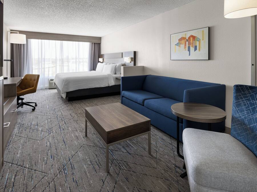 A hotel room with a bed, a sofa, a small table, a desk, and a chair.