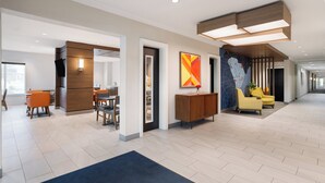 A modern hotel lobby with a reception desk, seating area, and a dining space.