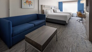 A hotel room with a blue sofa, a wooden coffee table, two beds, a desk, and a TV.
