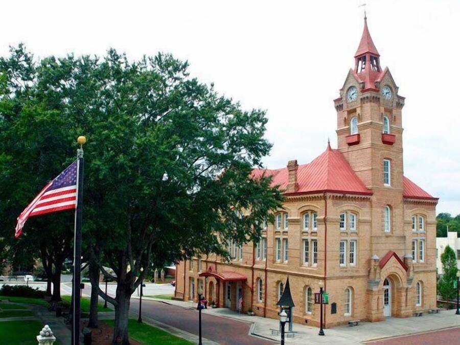 A historic building with a prominent clock tower, a flagpole with the American flag, and a well-maintained lawn.