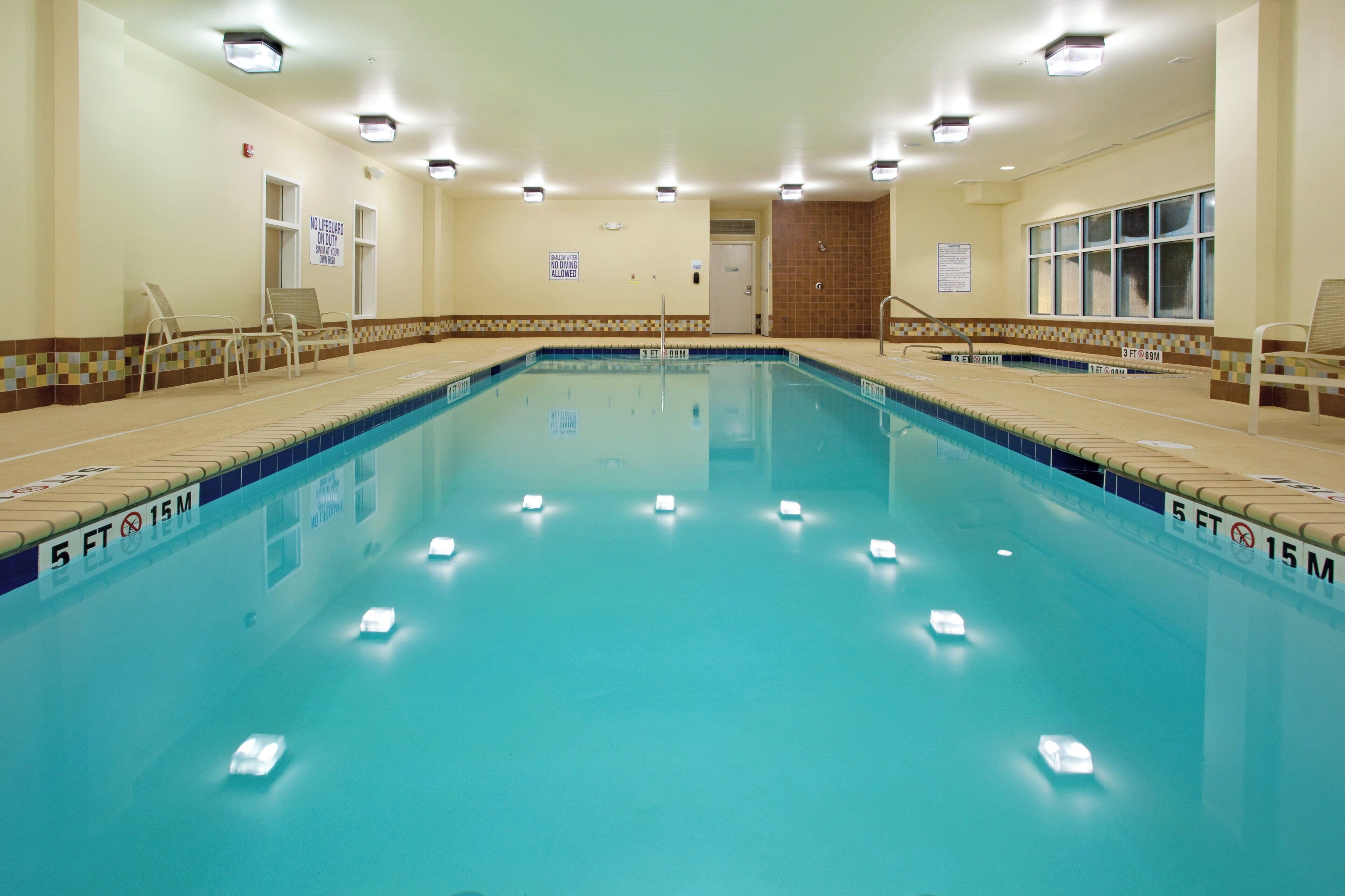 Una amplia piscina interior con marcas claras para carriles, señalización de seguridad y un borde de azulejos.