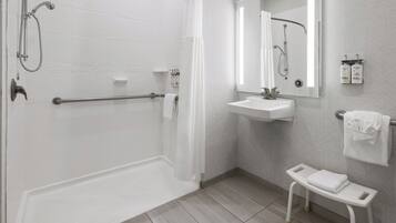 Un baño moderno con ducha a ras de suelo, lavabo, espejo y un pequeño banco.