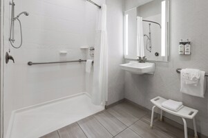 Un baño moderno con ducha a ras de suelo, lavabo, espejo y un pequeño banco.