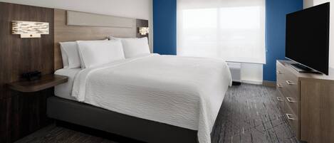 Een moderne hotelkamer met een groot bed, een flatscreen televisie, een nachtkastje en een raam met jaloezieën.