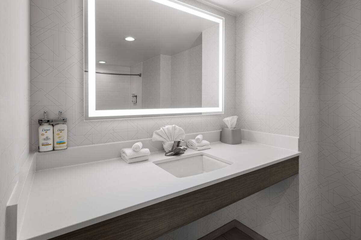 A modern bathroom with a large mirror, white countertop, and a wooden vanity.