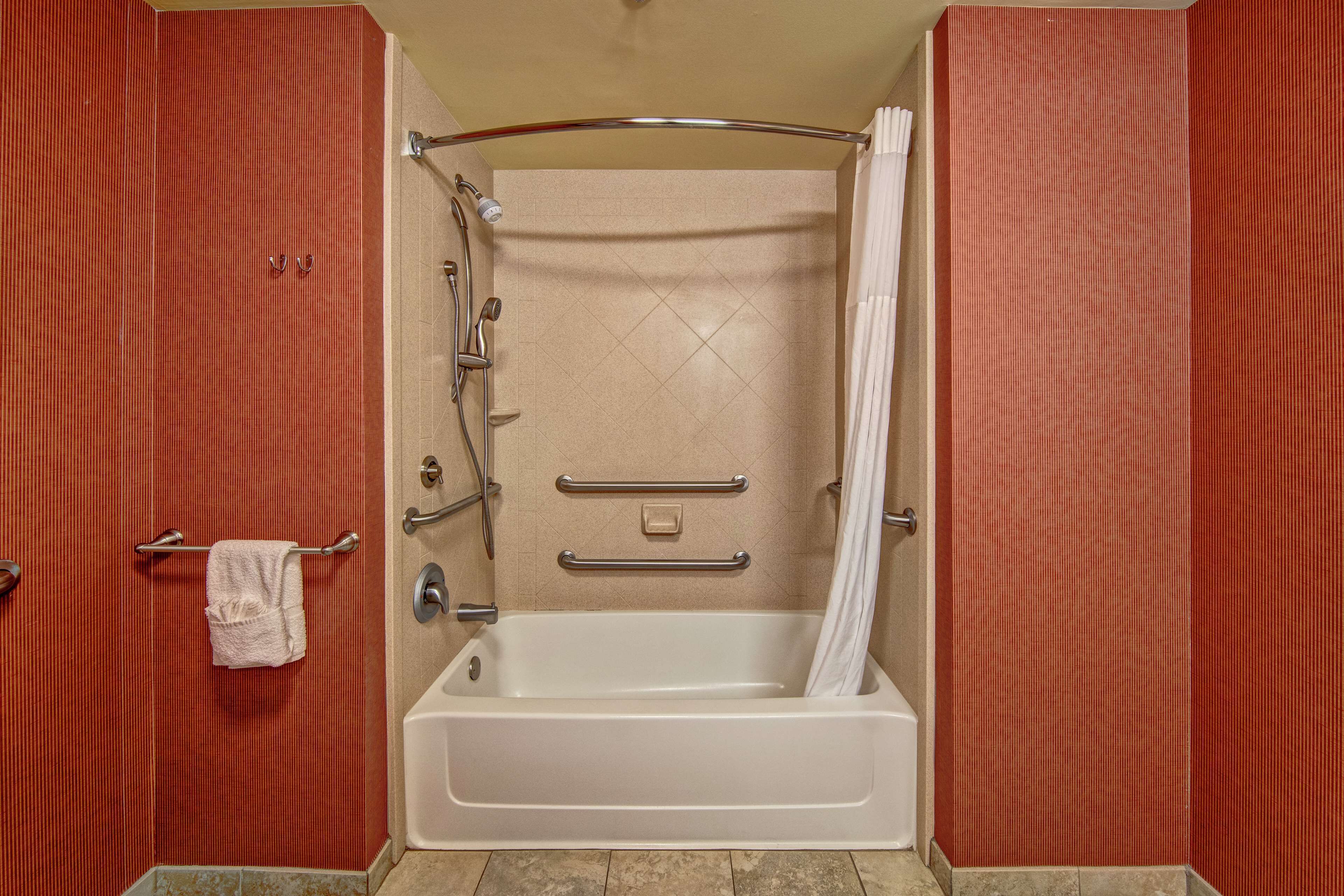 A bathroom with a bathtub, grab bars, and a towel rack.