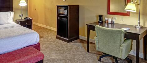 Une chambre d’hôtel équipée d’un lit, d’un bureau, d’une chaise, d’un mini-bar et d’une lampe.