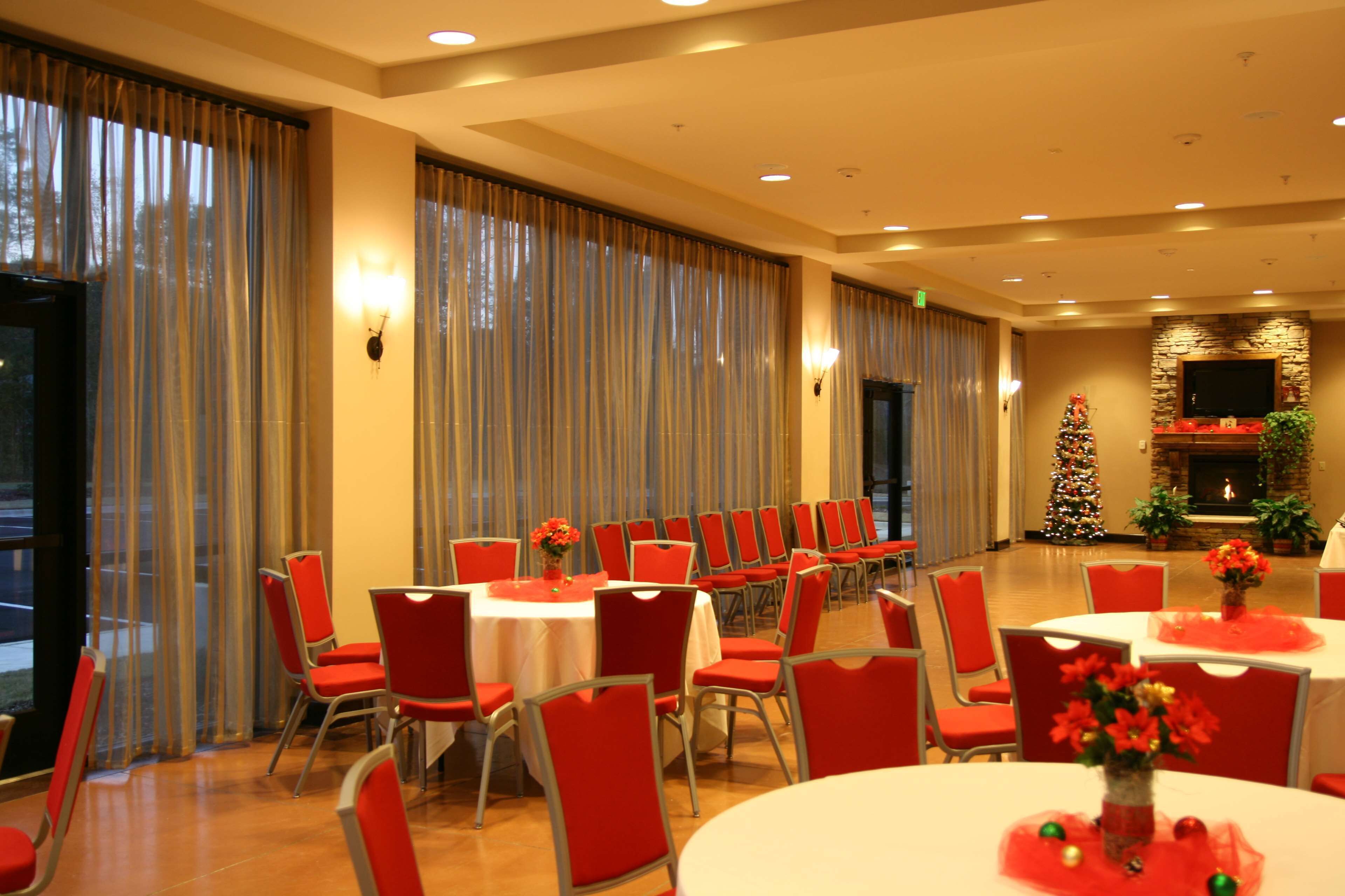 A spacious banquet hall with rows of red chairs and white tables, a Christmas tree, and a fireplace.