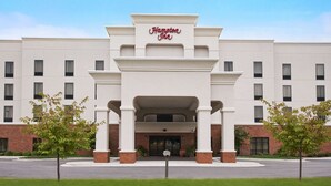 Un hotel Hampton Inn con fachada moderna, amplia entrada y zona de estacionamiento.