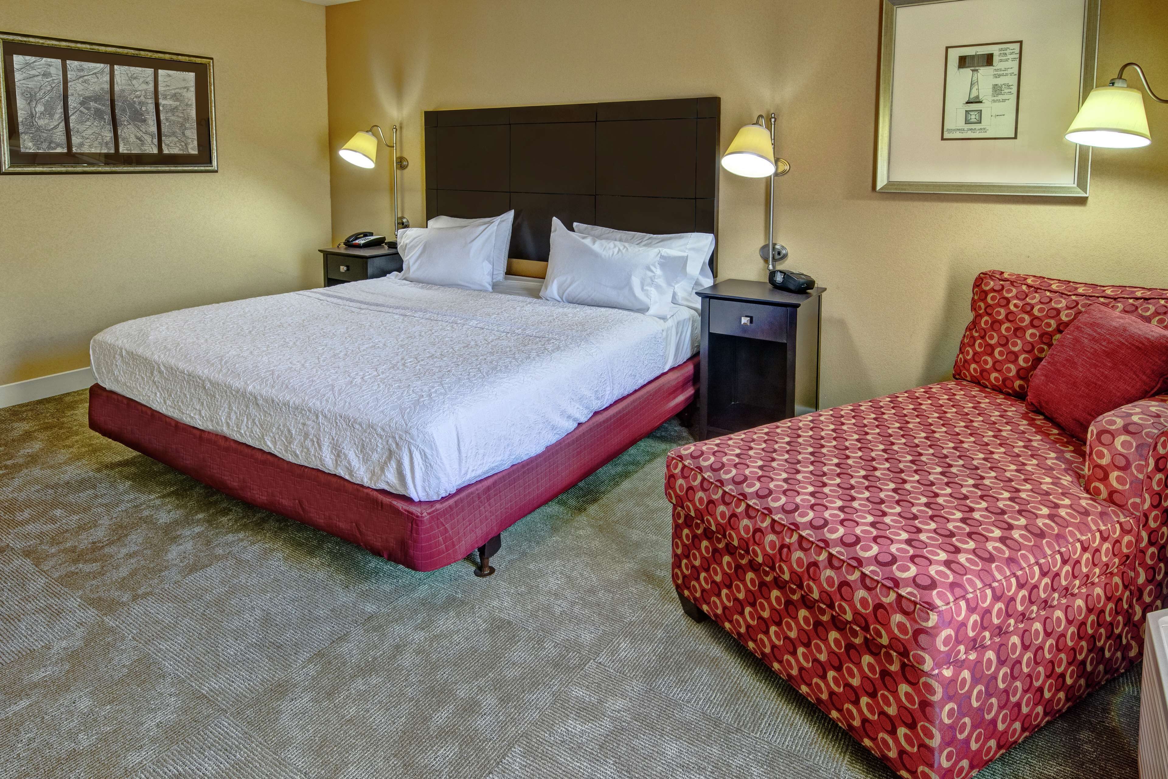 A hotel room with a large bed, two bedside tables, a red sofa, and two wall-mounted lamps.
