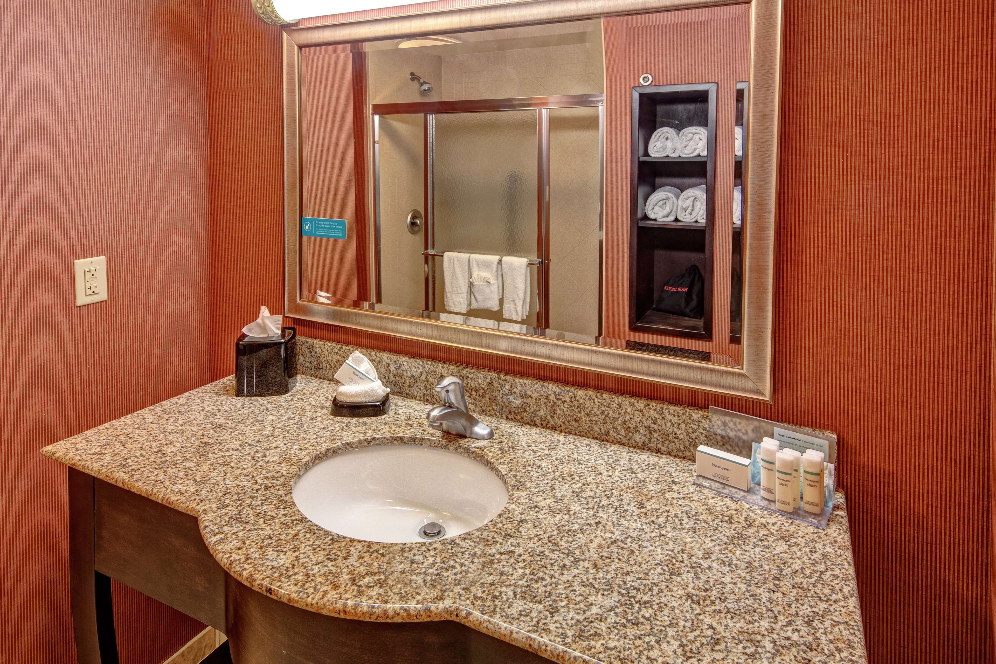A bathroom with a granite countertop sink, a mirror, and a towel rack with towels.