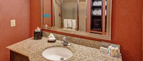 A bathroom with a granite countertop sink, a mirror, and a towel rack with towels.