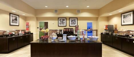 A spacious breakfast area with a central counter, various food stations, and framed pictures on the walls.