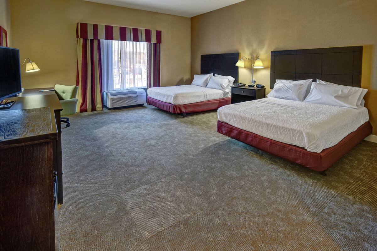 A hotel room with two beds, a desk, a chair, a TV, and a window with curtains.